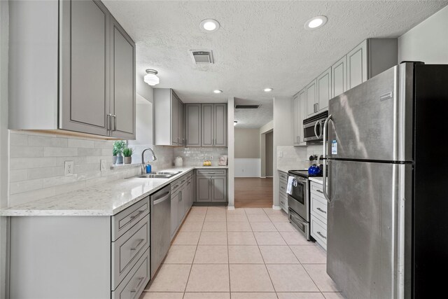 4131 N New Meadows Dr, Sugar Land, TX 77479 - kitchen featuring appliances with stainless steel finishes, a sink, gray cabinetry, a textured ceiling, and tasteful backsplash