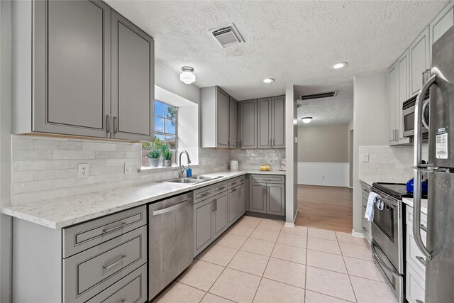 4131 N New Meadows Dr, Sugar Land, TX 77479 - kitchen featuring stainless steel appliances, gray cabinets, a textured ceiling, a sink, and decorative backsplash