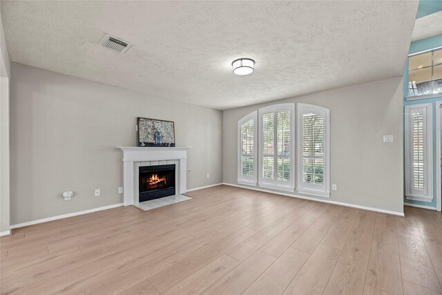 4131 N New Meadows Dr, Sugar Land, TX 77479 - unfurnished living room with a tiled fireplace, light wood-style flooring, plenty of natural light, a textured ceiling, and baseboards