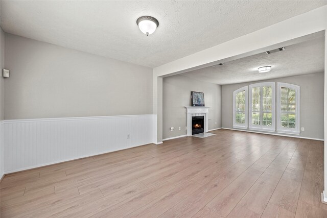 4131 N New Meadows Dr, Sugar Land, TX 77479 - unfurnished living room featuring wood finished floors, a textured ceiling, a fireplace with flush hearth, and a wainscoted wall