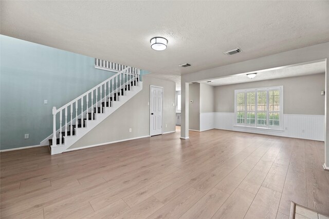 4131 N New Meadows Dr, Sugar Land, TX 77479 - unfurnished living room with stairs, light wood-style flooring, a textured ceiling, and wainscoting
