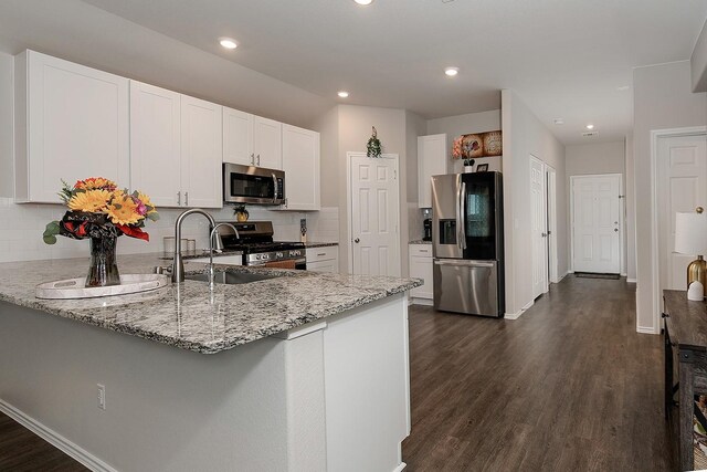 309 Cumberland Forest Dr, Magnolia, TX 77354 - kitchen with stainless steel appliances, a peninsula, light stone counters, white cabinets, and backsplash