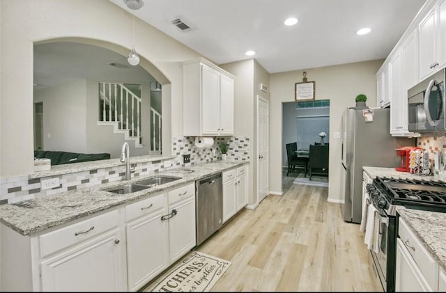 5732 Montclair Hill Ln, Rosharon, TX 77583 - kitchen with stainless steel appliances, decorative backsplash, white cabinetry, light wood finished floors, and arched walkways