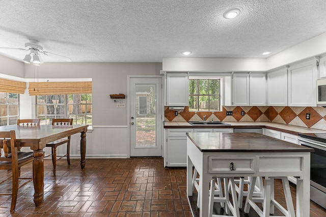 457 Monticello Park, Conroe, TX 77302 - kitchen featuring electric stove, a textured ceiling, white microwave, a sink, and brick floors