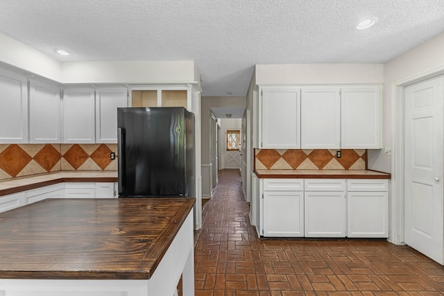 457 Monticello Park, Conroe, TX 77302 - kitchen featuring freestanding refrigerator, wood counters, brick floors, a textured ceiling, and decorative backsplash