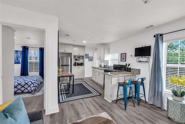 7112 Ave L, Houston, TX 77011 - kitchen with freestanding refrigerator, white cabinetry, a breakfast bar area, wood finished floors, and recessed lighting