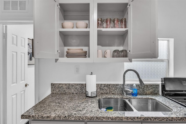 7112 Ave L, Houston, TX 77011 - kitchen view of open shelves, a sink, light stone countertops, and white cabinetry