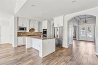 27684 Rio Blanco Dr, Splendora, TX 77372 - kitchen featuring arched walkways, white microwave, a kitchen island with sink, dark wood finished floors, and white cabinets