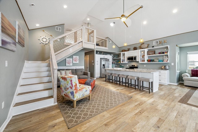 219 Bora Bora Dr, Tiki Island, TX 77554 - living room featuring high vaulted ceiling, stairs, ceiling fan, light wood-style flooring, and baseboards
