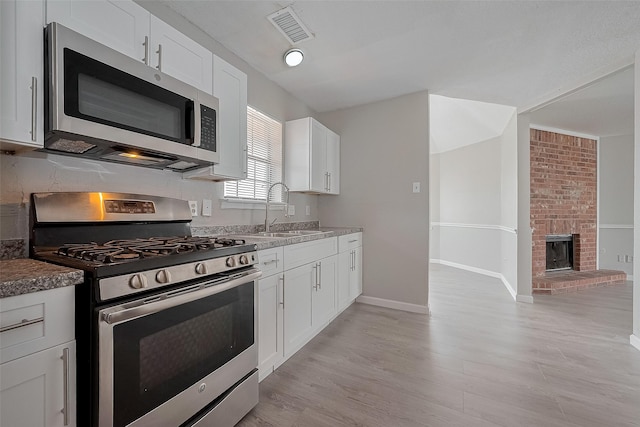 8621 Rustling Lvs Dr, Houston, TX 77083 - kitchen with appliances with stainless steel finishes, a sink, light wood-style flooring, white cabinetry, and baseboards