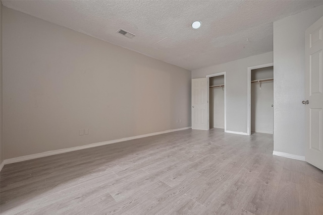 8621 Rustling Lvs Dr, Houston, TX 77083 - unfurnished bedroom featuring light wood finished floors, a textured ceiling, two closets, and baseboards