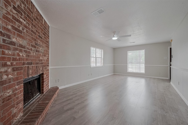 8621 Rustling Lvs Dr, Houston, TX 77083 - unfurnished living room with ceiling fan, a textured ceiling, a fireplace, wood finished floors, and a wainscoted wall