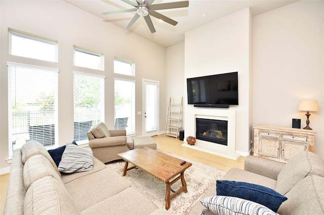 22911 Pearl Glen Dr, Richmond, TX 77469 - living room featuring a ceiling fan, light wood finished floors, a glass covered fireplace, a high ceiling, and baseboards