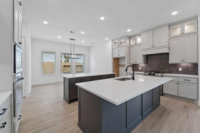 12834 Forest Garden Ct, Conroe, TX 77302 - kitchen with appliances with stainless steel finishes, a sink, a center island with sink, light wood finished floors, and tasteful backsplash
