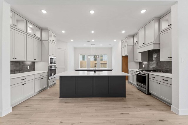 12834 Forest Garden Ct, Conroe, TX 77302 - kitchen featuring appliances with stainless steel finishes, a sink, tasteful backsplash, a kitchen island with sink, and glass insert cabinets