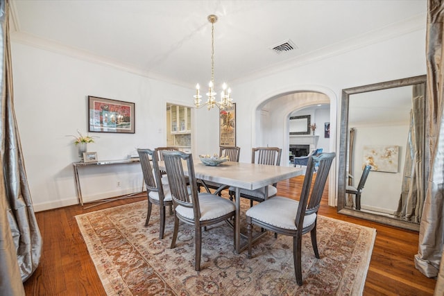 2256 Dryden Rd, Houston, TX 77030 - dining room with crown molding, arched walkways, a chandelier, a fireplace, and wood finished floors