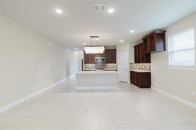 16719 Highland Country Dr, Cypress, TX 77433 - kitchen featuring stainless steel microwave, tasteful backsplash, light countertops, recessed lighting, and a center island with sink
