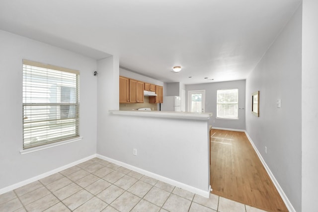 12047 Madison Oak St, Houston, TX 77038 - kitchen featuring freestanding refrigerator, a peninsula, under cabinet range hood, baseboards, and light countertops