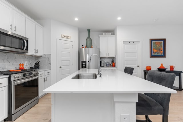 30114 Ousel Falls Ln, Fulshear, TX 77494 - kitchen featuring appliances with stainless steel finishes, a sink, light wood-type flooring, decorative backsplash, and a breakfast bar