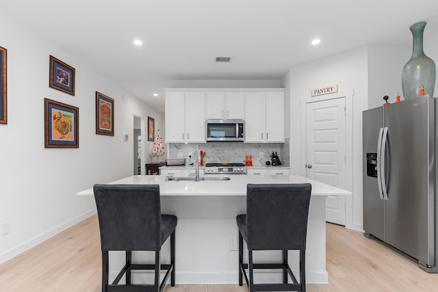 30114 Ousel Falls Ln, Fulshear, TX 77494 - kitchen with stainless steel appliances, backsplash, white cabinets, a kitchen breakfast bar, and light wood finished floors