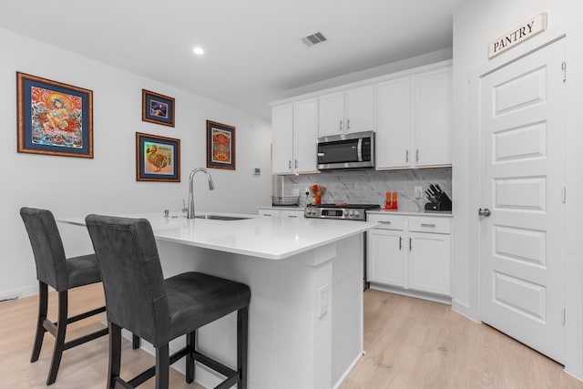 30114 Ousel Falls Ln, Fulshear, TX 77494 - kitchen featuring stainless steel microwave, light wood-type flooring, a sink, backsplash, and a kitchen breakfast bar