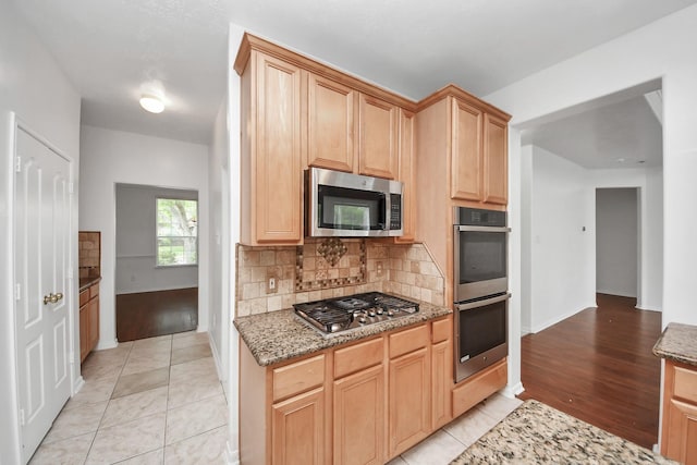 1605 Spring Glen Ln, Pearland, TX 77581 - kitchen with stainless steel appliances, decorative backsplash, light stone countertops, baseboards, and light brown cabinetry