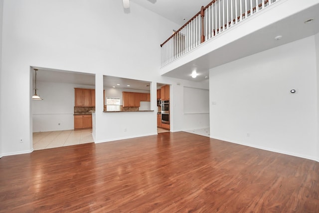 1605 Spring Glen Ln, Pearland, TX 77581 - unfurnished living room with light wood-type flooring, a ceiling fan, a high ceiling, and baseboards