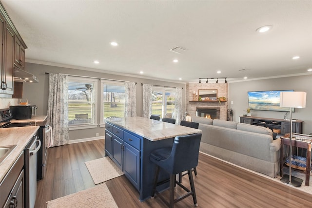 4620 Springfield Ln, Brenham, TX 77833 - kitchen featuring a brick fireplace, blue cabinetry, under cabinet range hood, crown molding, and a kitchen bar