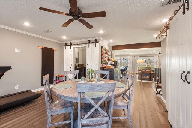 4620 Springfield Ln, Brenham, TX 77833 - dining room featuring a barn door, light wood-type flooring, ceiling fan, ornamental molding, and baseboards