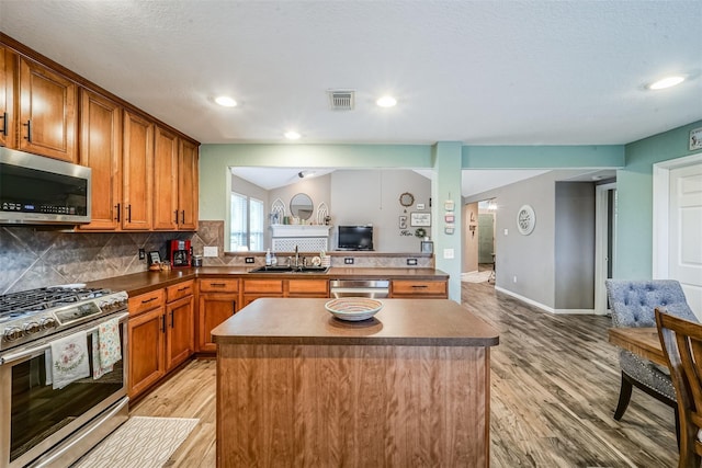 2957 Water Willow Ln, Pearland, TX 77581 - kitchen with appliances with stainless steel finishes, light wood-style flooring, a kitchen island, brown cabinets, and recessed lighting