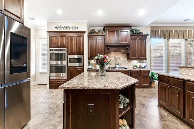 5702 Mustang Ridge Ln, Fulshear, TX 77441 - kitchen featuring stainless steel appliances, tasteful backsplash, dark brown cabinetry, light stone counters, and a center island