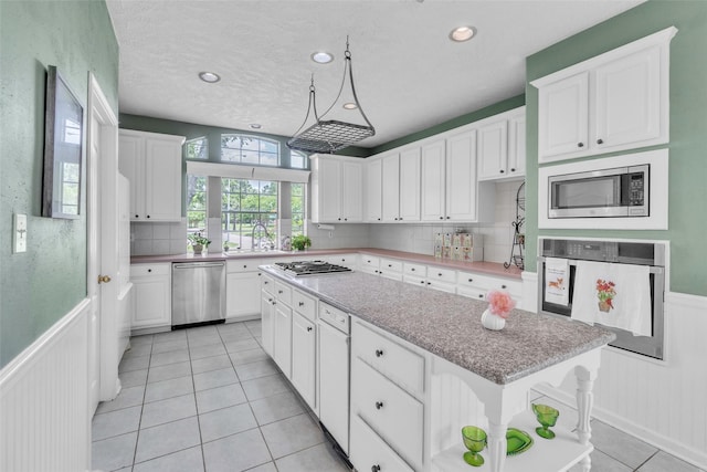 17503 Whispering Star Ct, Houston, TX 77095 - kitchen featuring stainless steel appliances, wainscoting, a kitchen island, white cabinetry, and light tile patterned flooring
