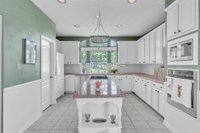 17503 Whispering Star Ct, Houston, TX 77095 - kitchen featuring stainless steel appliances, a center island, white cabinetry, light tile patterned flooring, and a wainscoted wall