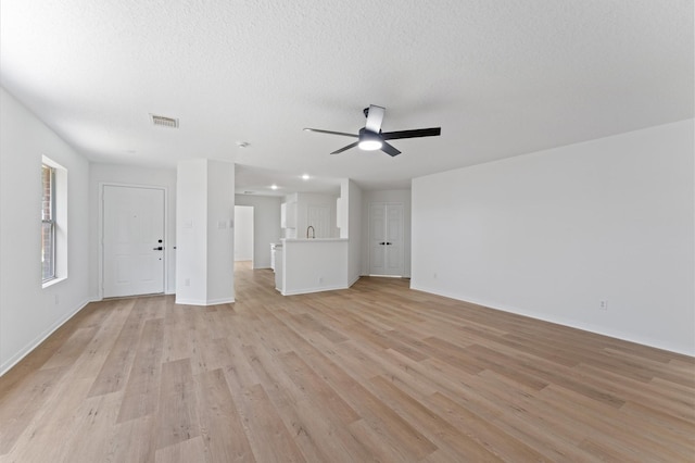 2411 Irish Spring Dr, Houston, TX 77067 - unfurnished living room featuring light wood finished floors, a ceiling fan, baseboards, and a textured ceiling