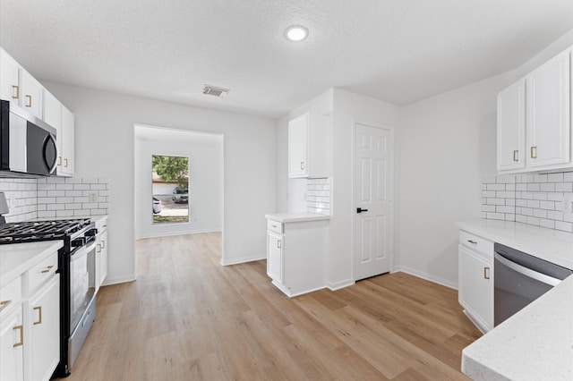 2411 Irish Spring Dr, Houston, TX 77067 - kitchen with appliances with stainless steel finishes, backsplash, white cabinetry, light wood finished floors, and a textured ceiling