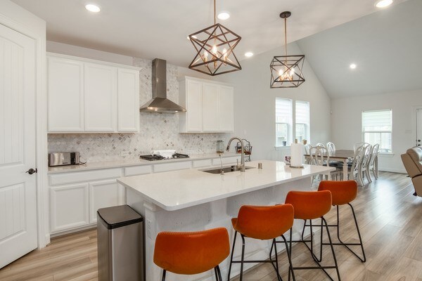 11211 Stirton, Tomball, TX 77375 - kitchen featuring wall chimney exhaust hood, a sink, decorative backsplash, an island with sink, and a breakfast bar