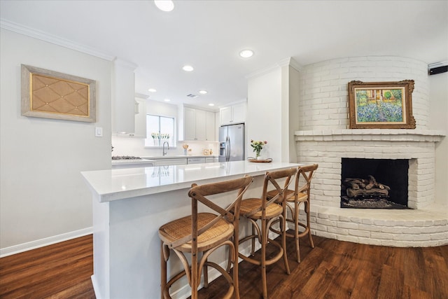 2910 Ann Arbor Dr, Houston, TX 77063 - kitchen with stainless steel fridge, dark wood-type flooring, light countertops, a breakfast bar area, and white cabinets