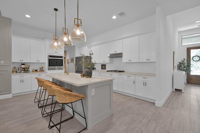 4792 W Fork Blvd, Conroe, TX 77304 - kitchen with oven, under cabinet range hood, tasteful backsplash, a kitchen bar, and a kitchen island with sink