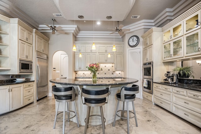 11 Bracebridge Dr, The Woodlands, TX 77382 - kitchen with a ceiling fan, built in appliances, cream cabinetry, tasteful backsplash, and a kitchen bar