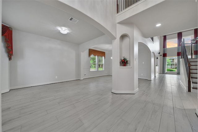 17862 Camp Cove Dr, Cypress, TX 77429 - empty room featuring arched walkways, wood finished floors, stairs, a towering ceiling, and baseboards