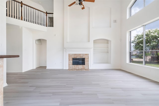 14339 Tasmania Ct, Sugar Land, TX 77498 - unfurnished living room featuring a tile fireplace, a towering ceiling, a ceiling fan, wood finished floors, and built in shelves