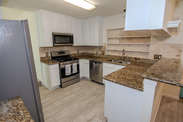 17647 Seven Pines Dr, Spring, TX 77379 - kitchen featuring stainless steel appliances, a sink, a peninsula, dark stone countertops, and a textured ceiling