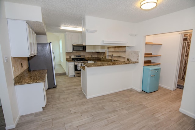 17647 Seven Pines Dr, Spring, TX 77379 - kitchen with appliances with stainless steel finishes, a peninsula, a textured ceiling, white cabinetry, and light wood finished floors