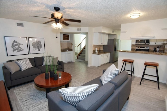 17647 Seven Pines Dr, Spring, TX 77379 - living area with light wood-style flooring, a textured ceiling, ceiling fan, and stairs