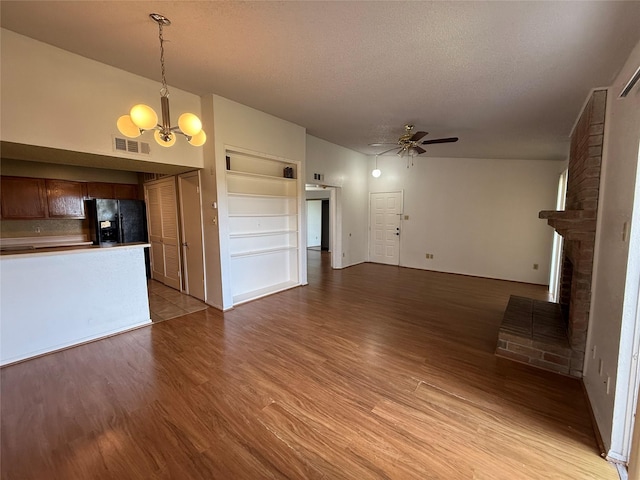 10555 Turtlewood Ct Unit 2011, Houston, TX 77072 - unfurnished living room featuring ceiling fan, a chandelier, a brick fireplace, light wood-style floors, and a textured ceiling