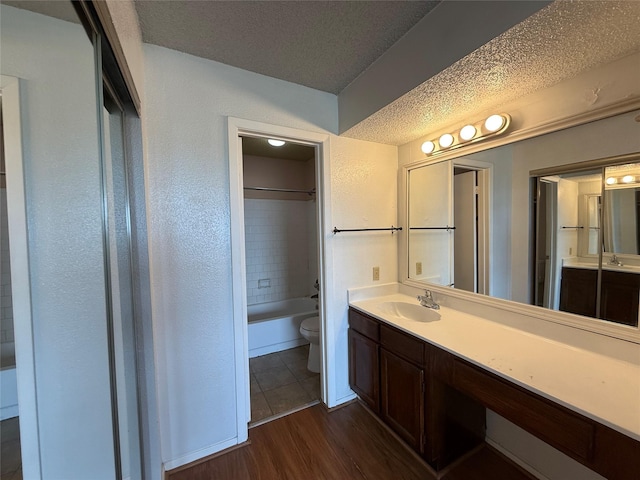 10555 Turtlewood Ct Unit 2011, Houston, TX 77072 - bathroom featuring toilet, a textured ceiling, vanity, wood finished floors, and washtub / shower combination