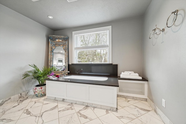 2108 Branard St, Houston, TX 77098 - bathroom featuring marble look tiles, a textured ceiling, a garden tub, and baseboards