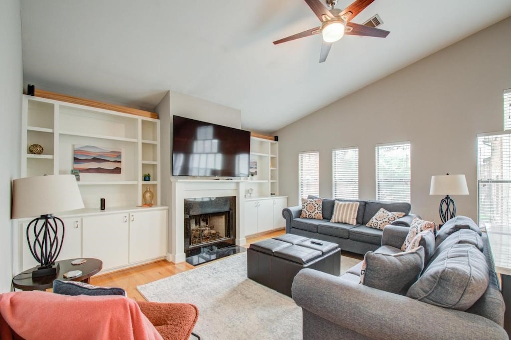 9705 Riddlewood Ln, Houston, TX 77025 - living area featuring light wood-type flooring, a fireplace with flush hearth, ceiling fan, and high vaulted ceiling