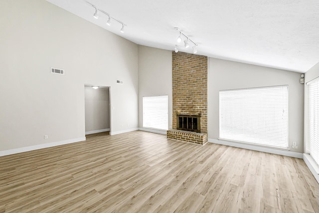 12014 Briar Forest Dr, Houston, TX 77077 - unfurnished living room with track lighting, lofted ceiling, light wood finished floors, a brick fireplace, and baseboards