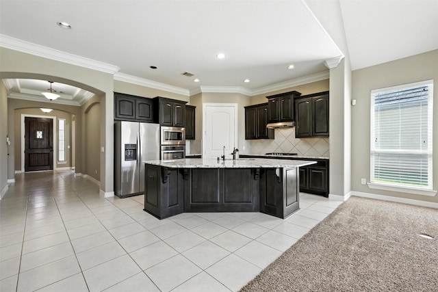 4914 Fairford Dr, Sugar Land, TX 77479 - kitchen featuring stainless steel appliances, light tile patterned floors, arched walkways, a breakfast bar, and a kitchen island with sink